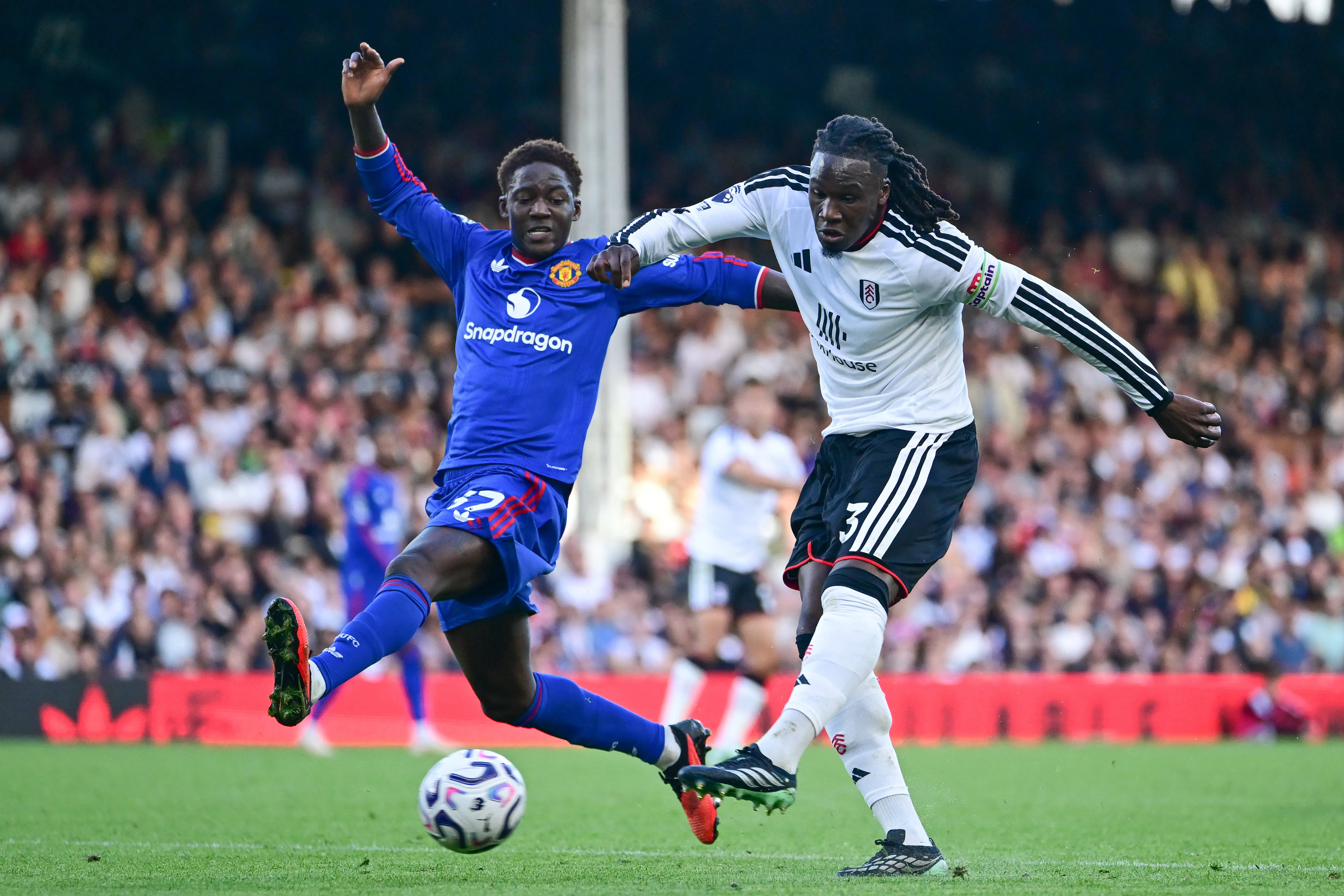 Fulham captain Calvin Bassey takes a shot at goal under pressure from Manchester United midfielder Kobbie Mainoo