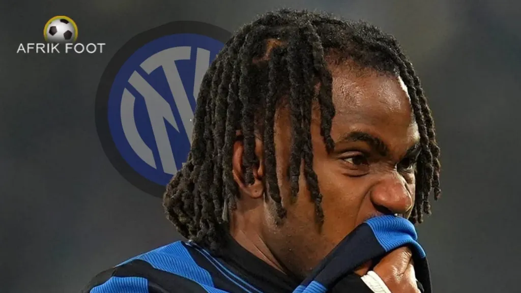 a photo of ademola lookman wiping his mouth on his jersey, with the inter badge, fading, behind his head